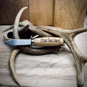 May include: A small, personalized knife with a wooden handle and a stainless steel blade. The knife is resting on a pile of antlers. The handle is engraved with the text "[Your Text Here]".