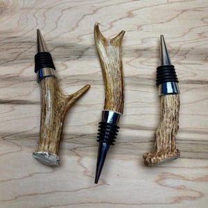 Può includere: Tre tappi per bottiglie in corno di cervo con tappi argentati e guarnizioni in gomma nera. Il corno di cervo è di colore marrone naturale.