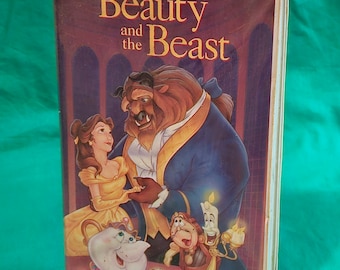 Puede incluir: Una caja de cinta VHS con la clásica película de Disney "La Bella y la Bestia". La portada muestra a Bella y la Bestia de pie juntos, con otros personajes de la película, incluyendo Lumiere, la Sra. Potts y Chip, en el fondo.