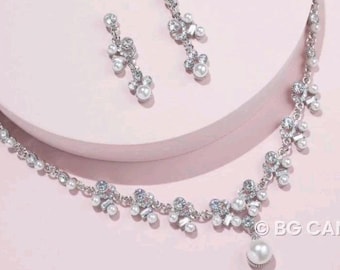 May include: A silver necklace and earrings set with a pearl pendant and crystal accents. The necklace has a delicate chain with a cluster of pearls and crystals.