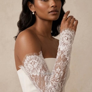 May include: Elegant white lace bridal sleeves featuring a floral design. The sleeves are long and fitted, with a delicate, scalloped edge. The intricate lace detailing adds a touch of sophistication. Ideal for a wedding or special event.