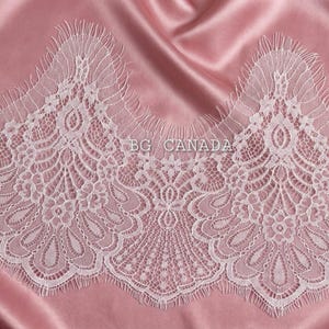 May include: White lace trim with a scalloped edge, featuring intricate floral and geometric patterns. The lace is set against a pink satin background. The text "BG CANADA" is visible on the lace.