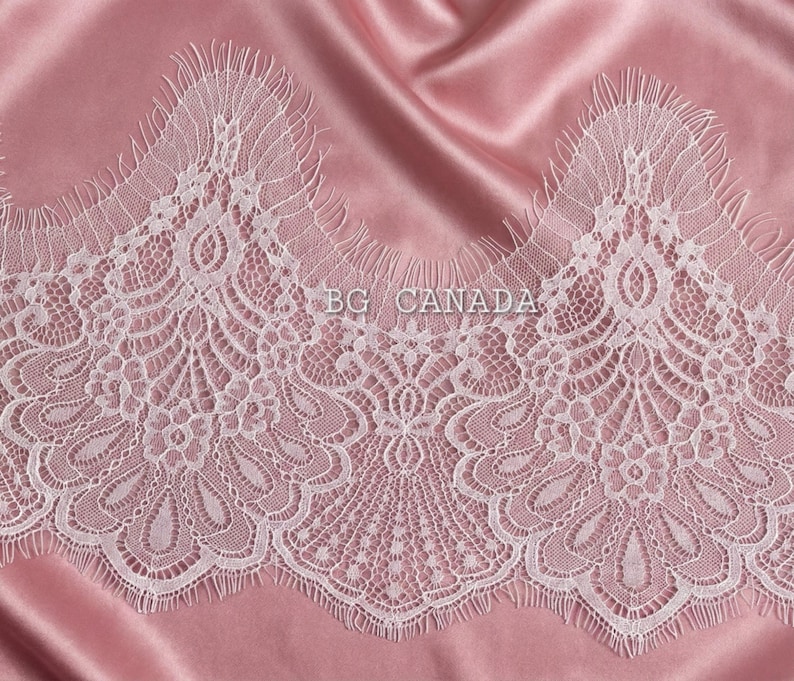 May include: White lace trim with a scalloped edge, featuring intricate floral and geometric patterns. The lace is set against a pink satin background. The text "BG CANADA" is visible on the lace.