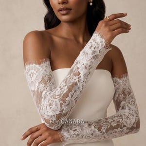 May include: White lace bridal sleeves with floral patterns. The sleeves are long and fitted, with a delicate fringe at the edges. The text "BG CANADA" is visible on the sleeve.