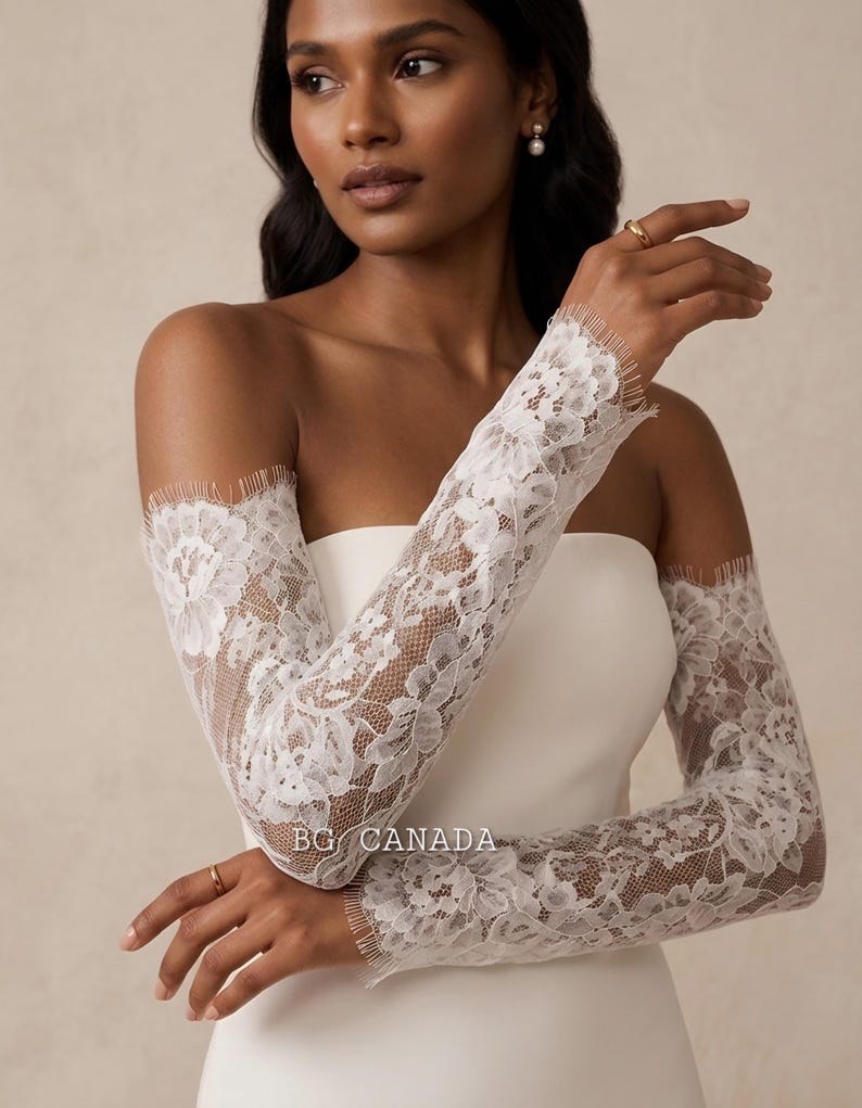 May include: White lace bridal sleeves with floral patterns. The sleeves are long and fitted, with a delicate fringe at the edges. The text "BG CANADA" is visible on the sleeve.