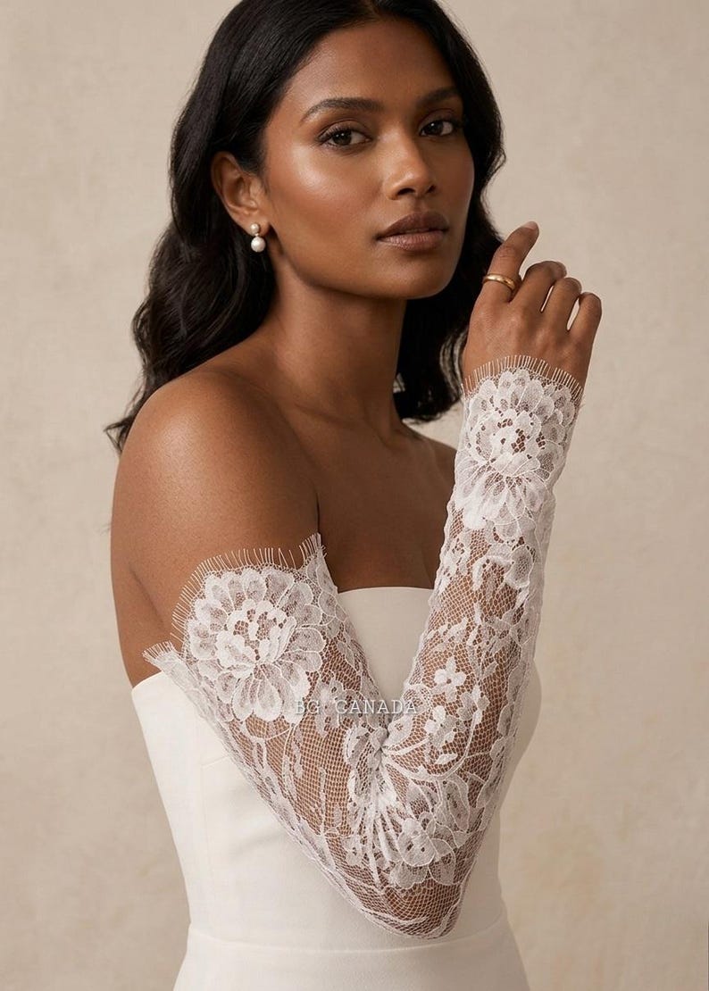 May include: Elegant white lace bridal sleeves featuring a floral design. The sleeves are long and fitted, with a delicate, scalloped edge. The intricate lace detailing adds a touch of sophistication. Ideal for a wedding or special event.