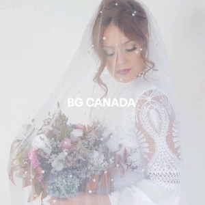 May include: A bride wearing a white lace dress and a veil with pearl accents holds a bouquet of dried flowers. The text "BG CANADA" is visible in the image.