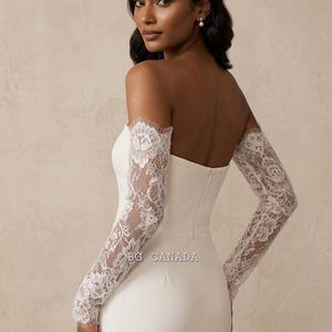 May include: A white strapless wedding dress with long lace sleeves. The sleeves are detailed and cover the arms from the shoulders to the wrists. The dress has a fitted bodice and a simple design. The text "BG CANADA" is visible.