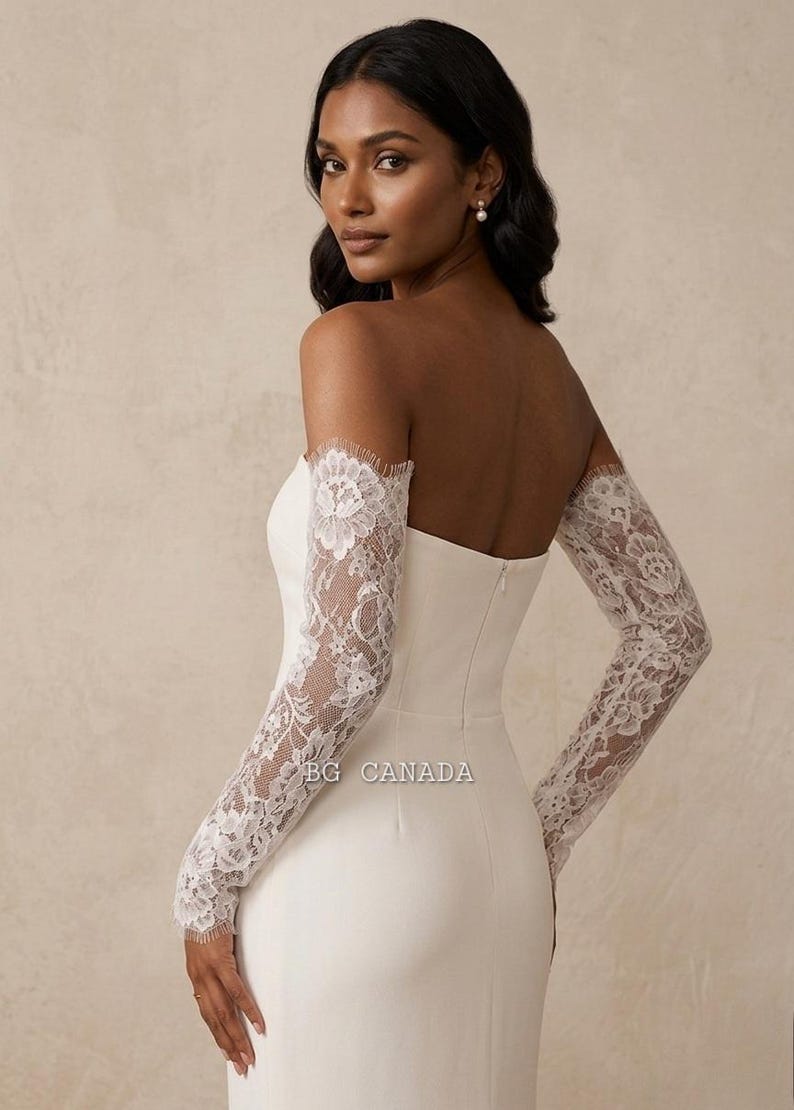 May include: A white strapless wedding dress with long lace sleeves. The sleeves are detailed and cover the arms from the shoulders to the wrists. The dress has a fitted bodice and a simple design. The text "BG CANADA" is visible.
