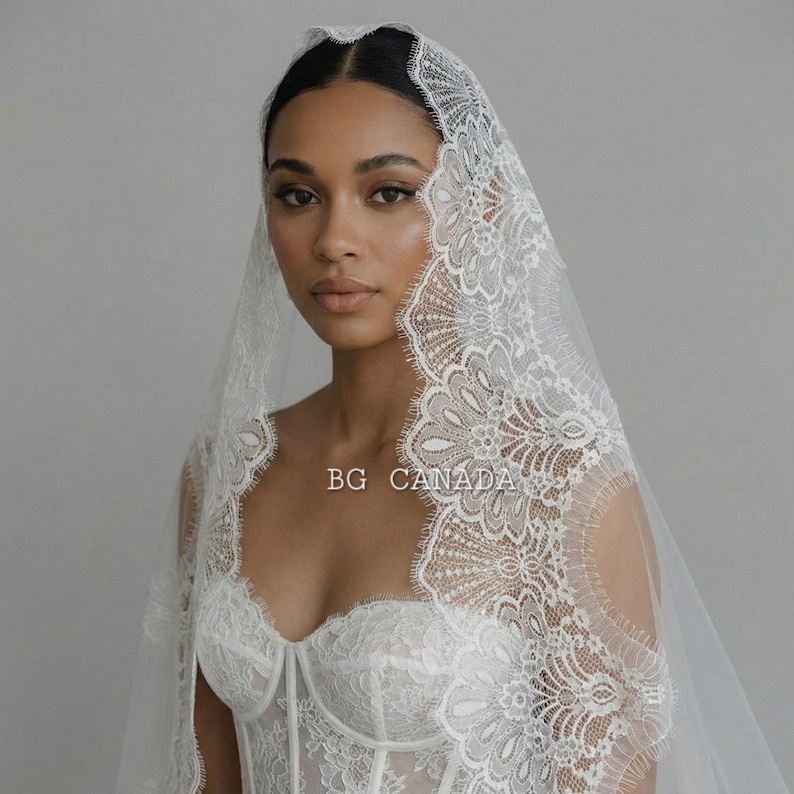 May include: A white lace bridal veil with intricate floral patterns and scalloped edges. The veil is draped over a white lace bodice. The text "BG CANADA" is visible on the image.