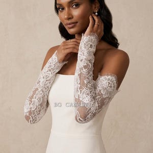 May include: White lace bridal sleeves with a floral design. The sleeves are long and fitted, covering the arms from the shoulders to the wrists. The sleeves are worn with a white strapless dress. The text "BG CANADA" is visible.