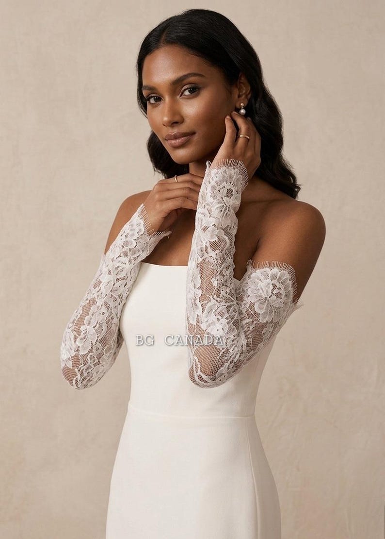 May include: White lace bridal sleeves with a floral design. The sleeves are long and fitted, covering the arms from the shoulders to the wrists. The sleeves are worn with a white strapless dress. The text "BG CANADA" is visible.