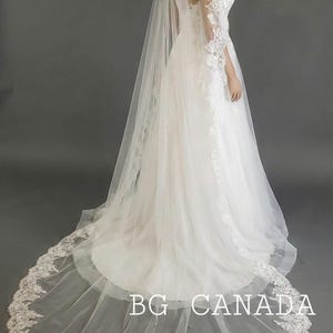 May include: A white wedding dress with a long train and a matching veil. The veil and dress are adorned with delicate lace detailing. The text "BG CANADA" is visible on the train.