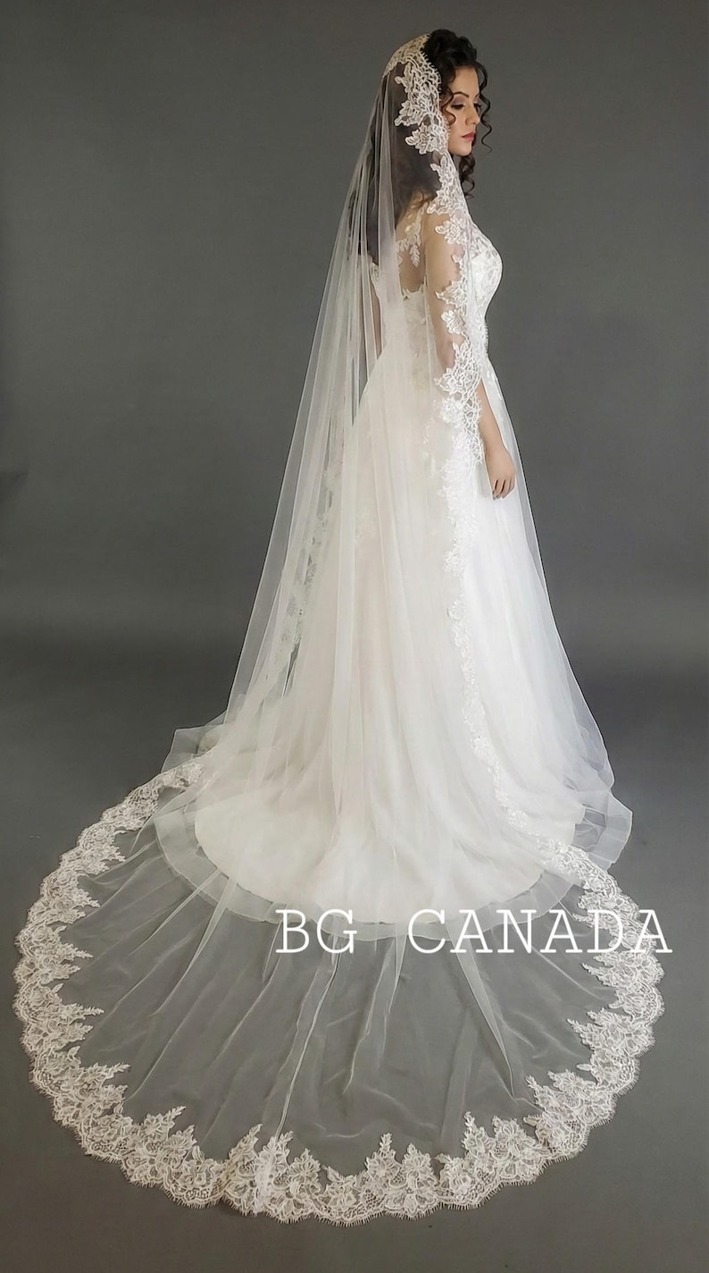 May include: A white wedding dress with a long train and a matching veil. The veil and dress are adorned with delicate lace detailing. The text "BG CANADA" is visible on the train.