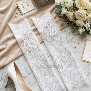 May include: A bridal flat lay featuring white lace arm sleeves, a pair of white high heels, a bouquet of white flowers, and a ring pillow with rings. Pearl earrings and loose pearls are also present.