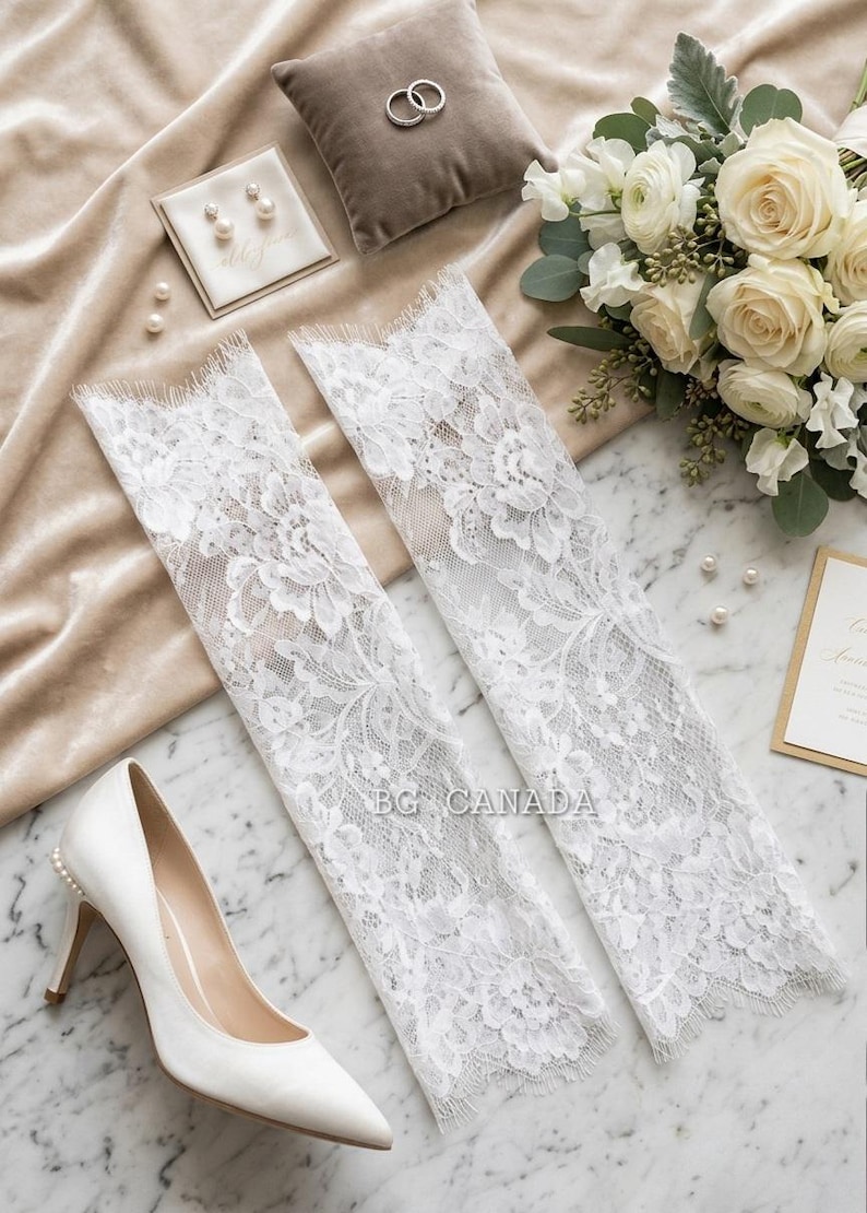 May include: A bridal flat lay featuring white lace arm sleeves, a pair of white high heels, a bouquet of white flowers, and a ring pillow with rings. Pearl earrings and loose pearls are also present.
