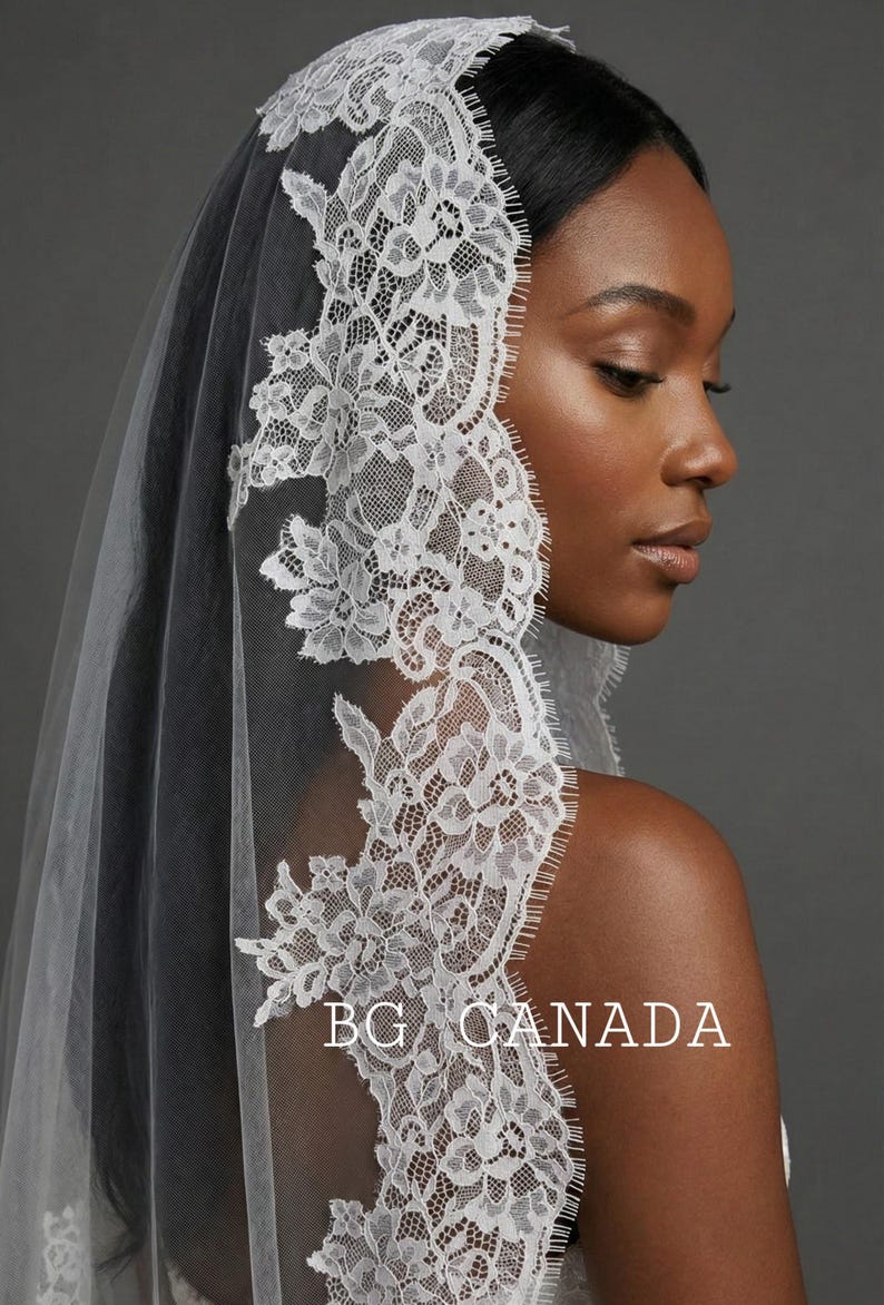 May include: A white lace bridal veil with intricate floral and leaf patterns. The veil is draped over the head and shoulders, with the text "BG CANADA" visible. The veil's delicate design adds a touch of elegance.