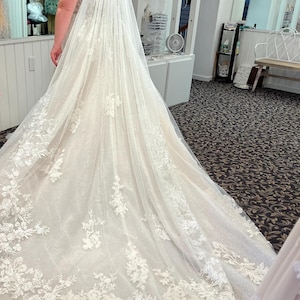Pode incluir: Um vestido de noiva branco com uma cauda longa e detalhes delicados de renda floral. O vestido é combinado com um véu de tule branco. O letreiro no fundo diz "Eu disse SIM ao vestido!"