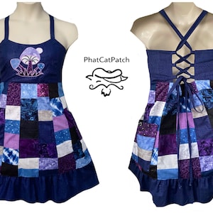 May include: A patchwork dress featuring a dark blue bodice with an embroidered purple mushroom design and the text PhatCatPatch. The skirt consists of various blue, purple, and black fabric squares with a ruffled hem and a lace-up back closure.