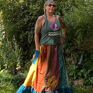 May include: A woman wearing a green tank top with the text "Deadheads for Kamala" and a colorful patchwork skirt. The skirt features panels of yellow, orange, burgundy, and teal fabrics with a ruffled hem.