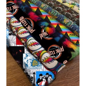 May include: A collection of fabric scraps featuring various band logos, including Pink Floyd, Grateful Dead, The Who, and The Beatles. The fabrics are colorful and feature a variety of patterns.