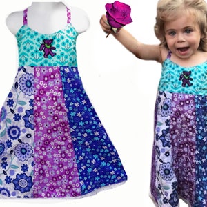 May include: A purple and blue patchwork dress with a tie-dye top and a purple bear graphic. The dress has a white lace trim.