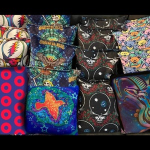 May include: A collection of decorative throw pillows with various designs. Pillows feature vibrant colors and patterns, including Grateful Dead imagery, dancing bears, and geometric shapes. The pillows are square and rectangular, suitable for home decor.