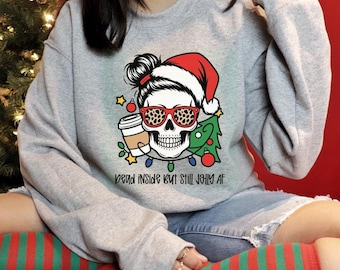 May include: A light gray sweatshirt featuring a skull wearing a Santa hat and leopard print glasses. The skull has a messy bun and is holding a coffee cup. A Christmas tree and string lights are also in the design. The text "Dead Inside But Still Jolly AF" is below the skull.