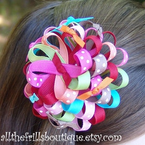 May include: A colorful hair bow made of multiple ribbons in various colors and patterns, including pink, red, green, blue, and white polka dots. The bow is tied into a large, fluffy knot and is perfect for adding a touch of whimsy to any hairstyle.