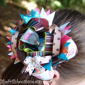 May include: A large, colorful hair bow with a variety of patterned ribbons, including brown and white stripes, brown and white polka dots, and blue and white polka dots. The bow also features a pink and blue owl print ribbon. The bow is tied in a large, fluffy knot and is perfect for adding a touch of whimsy to any outfit.