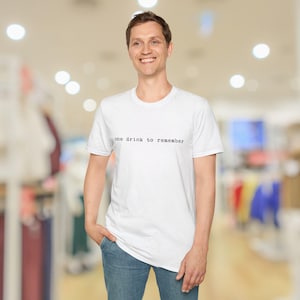 May include: A white ceramic mug with a black handle and the text "But First, Coffee" in a bold, black font. The mug is set against a blurred background, suggesting a cozy setting. The mug appears to be approximately 4 inches tall.