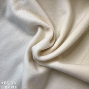 May include: Close-up of a soft, off-white fabric with a textured surface. The fabric is draped in gentle folds, creating shadows and highlights. The Tin Thimble logo is visible in the bottom left corner.