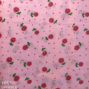 K&ouml;nnte beinhalten: Rosafarbener Stoff mit einem sich wiederholenden Muster aus kleinen roten Bl&uuml;ten mit gr&uuml;nen Stielen und Bl&auml;ttern. Der Hintergrund ist hellrosa mit kleinen roten Punkten.