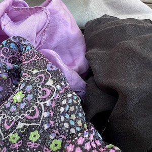 May include: A close-up of a pile of fabric scraps in various colors and patterns, including black, purple, and green. The fabric is soft and textured, and the colors are vibrant.