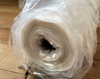 May include: A roll of clear plastic sheeting wrapped in a clear plastic bag. The sheeting is rolled tightly and is visible through the bag.