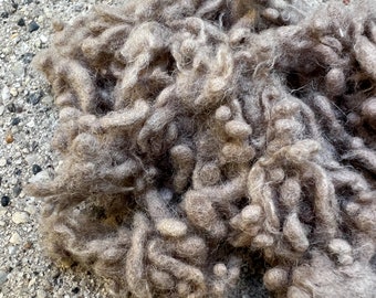 May include: A pile of brown wool yarn, with a soft, fluffy texture. The yarn is loosely packed and appears to be hand-spun.