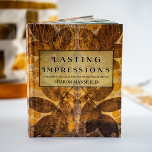 Può includere: Un libro intitolato "Lasting Impressions: A Practical Guide in the Art of Botanical Dyeing" di Sharon Mansfield. La copertina del libro presenta un motivo di foglie marroni e gialle.