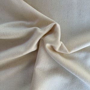 May include: Close-up of a cream-colored fabric with visible texture and folds. The fabric is a light, neutral tone, and the folds create shadows and depth. The text "THE TIN THIMBLE" is visible in the lower left corner.