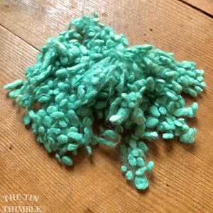 May include: A pile of teal blue yarn with fuzzy texture. The yarn is made of small, round balls of fiber.