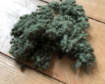 May include: A pile of dark green yarn fibers on a wooden surface.
