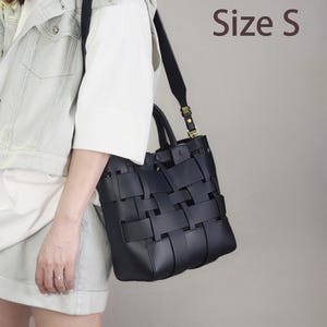 Puede incluir: Bolso tote de cuero negro tejido con una correa para el hombro. El bolso tiene un dise&ntilde;o estructurado con un patr&oacute;n tejido en la parte delantera y los lados. El texto "Size S" es visible en la imagen.