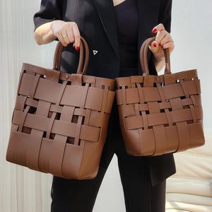 Puede incluir: Dos bolsos tote marrones tejidos con asas superiores. Las bolsas tienen forma rectangular y un dise&ntilde;o de tejido de cesta. Las bolsas son sostenidas por una persona que lleva una blazer negra y pantalones negros.