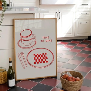 Könnte beinhalten: Kücheninterieur mit einem gerahmten Druck, der eine rote Strichzeichnung einer Tasse, eines Tellers, Besteck und den Text "TIME TO DINE" zeigt. Der Boden hat ein rot-schwarzes Schachbrettmuster. Ein Korb mit Äpfeln und eine Weinflasche sind ebenfalls zu sehen.