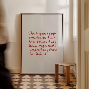 以下が含まれることがあります： 赤いインクで手書きされた「最も幸せな人々は、魔法が存在する場所を選ぶので、人生をロマンチックにする」という引用が書かれた白いポスターが額装されています。
