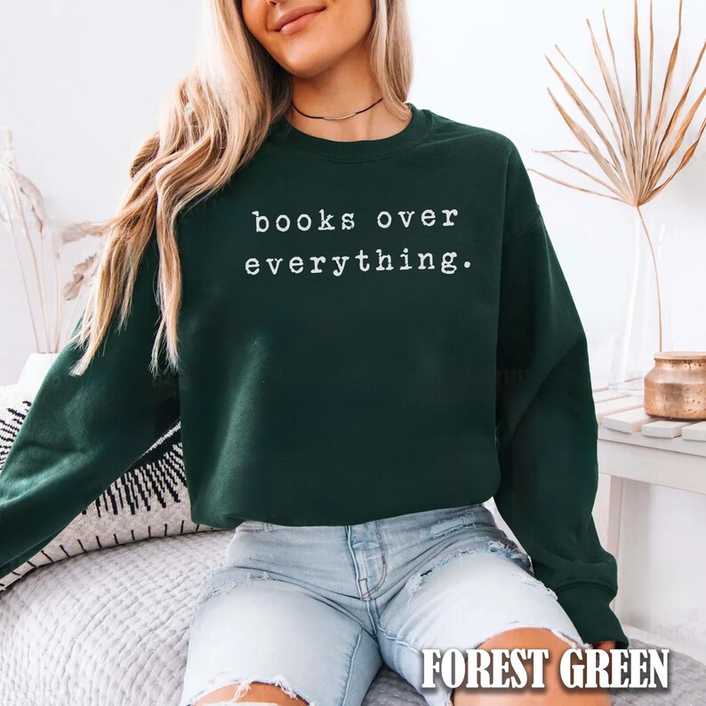 May include: Forest green sweatshirt with the text "books over everything" in white. The sweatshirt is a crew neck style and has long sleeves. The words "FOREST GREEN" are printed at the bottom of the image.