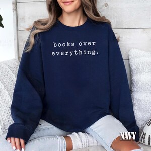 May include: Navy blue sweatshirt with the text "books over everything" in white. The sweatshirt is a crew neck style and has long sleeves. The word "NAVY" is printed at the bottom right corner of the image.