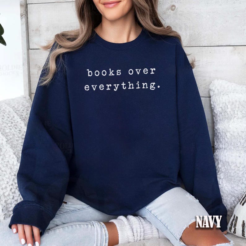 May include: Navy blue sweatshirt with the text "books over everything" in white. The sweatshirt is a crew neck style and has long sleeves. The word "NAVY" is printed at the bottom right corner of the image.