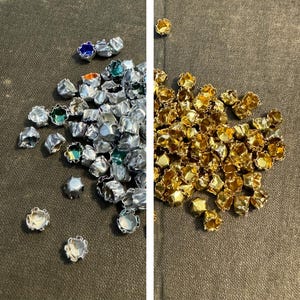 Puede incluir: Primer plano de dos pilas de adornos metálicos. Una pila es plateada con acentos verdes y azules, y la otra pila es dorada.