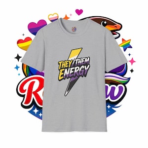 May include: A heather gray t-shirt with the text "THEY/THEM ENERGY" in yellow and purple, with a lightning bolt design. The shirt is surrounded by colorful Pride-themed graphics, including hearts and rainbows.