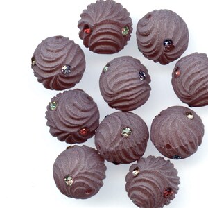 May include: A collection of ten dark brown, spherical beads with a textured, swirled design. Each bead is adorned with small, colorful rhinestones. The beads are arranged on a white background, showcasing their intricate details and vibrant accents.